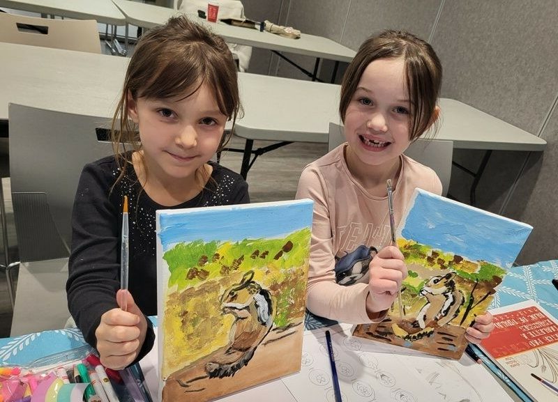 two girls with paintings from art class